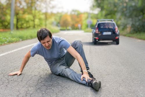 Man sitting on the road holding his lower leg