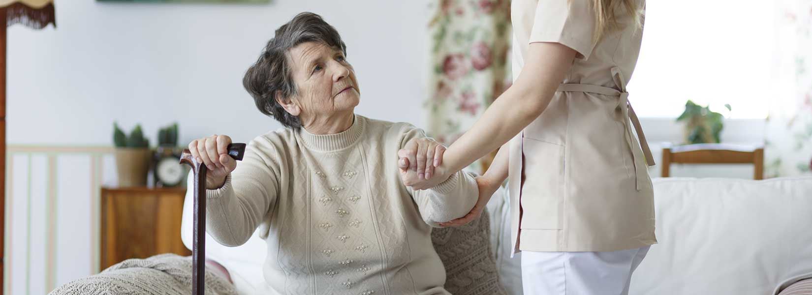 Elderly lady being helped up off the couch by her nurse