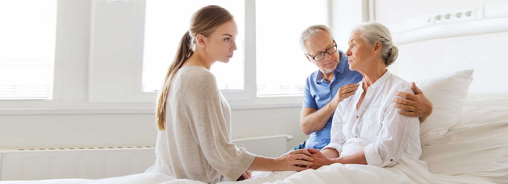 A nurse sitting on a bed comforting an elderly woman