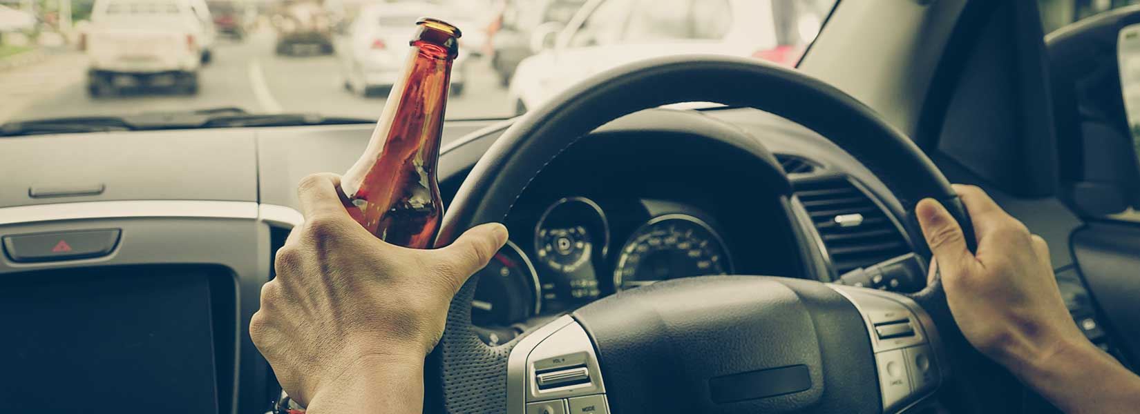 A person driving a car with a beer in their hand
