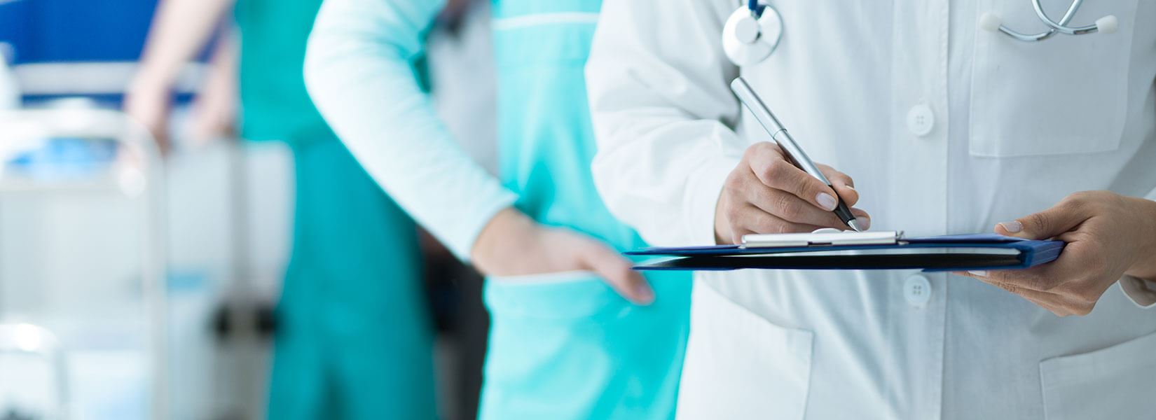 Doctors standing near eachother while one writes on a clipboard